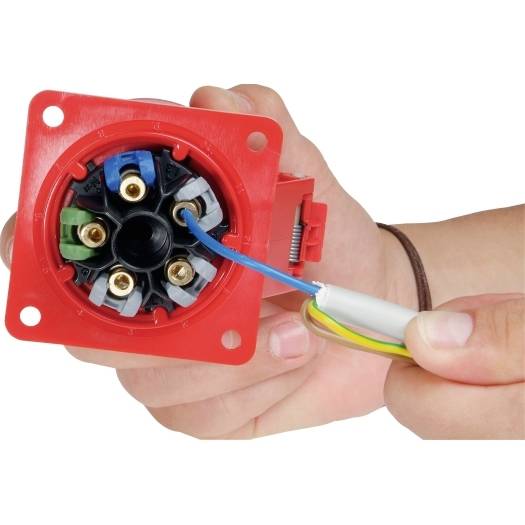 Hände verdrahten einen roten Elektrosteckerblock, wobei blaue und gelb-grüne Drähte in die Anschlüsse eingeführt werden.