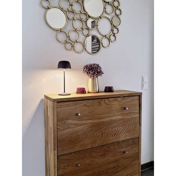 Holzschrank mit Lampe, Blumenvase und dekorativem rundem Wandspiegel darüber.