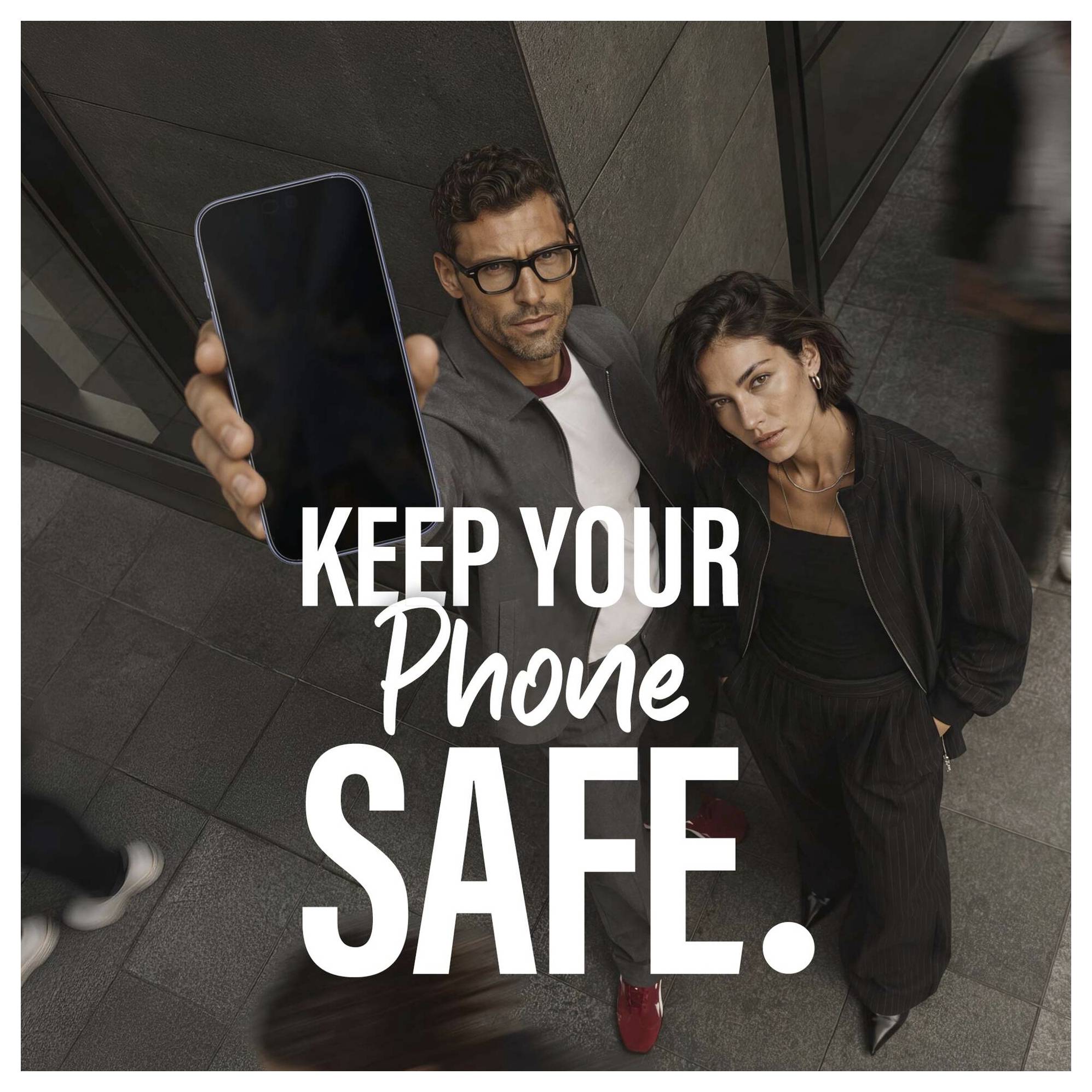 Zwei Menschen schauen in einer Stadtkulisse auf die Kamera, während einer ein Telefon hochhält; überlagterter Text lautet "KEEP YOUR Phone SAFE" (Schützen Sie Ihr Telefon).