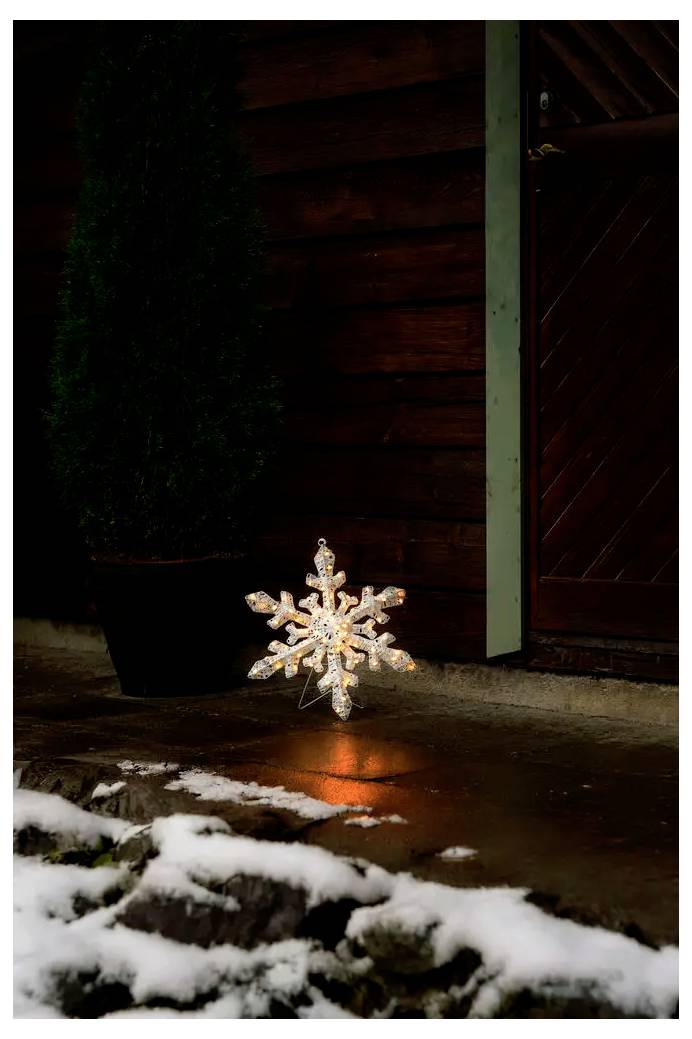 Leuchtende Schneeflocken-Dekoration glüht auf einer nassen Veranda neben einer Holztür, mit Schnee auf dem Boden im Vordergrund.