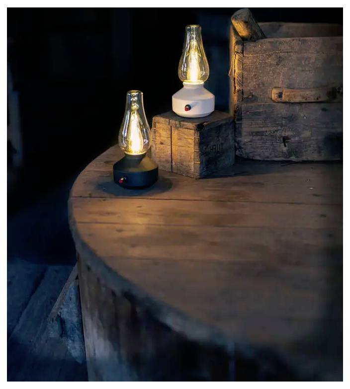 Zwei leuchtende Vintage-Laternen im alten Stil stehen auf gestapelten Holzkisten und einem runden Holztisch in einem dunklen, rustikalen Raum.