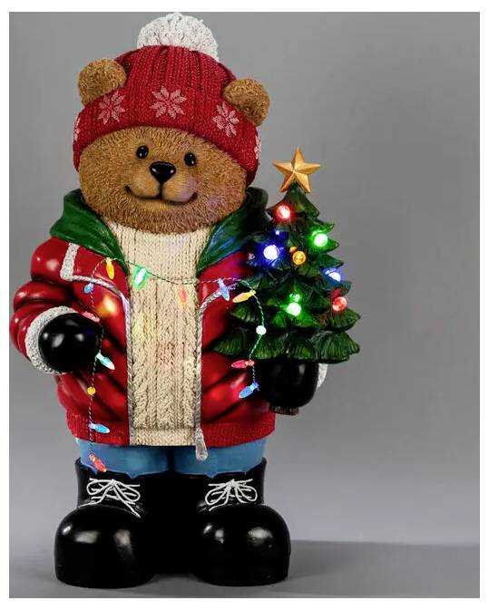 Eine Teddybär-Figur, gekleidet in einen roten Wintermantel und eine Strickmütze, hält einen leuchtenden Weihnachtsbaum mit einem goldenen Stern.