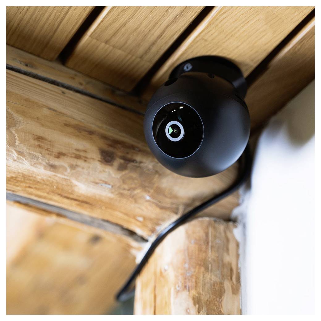 Schwarze Überwachungskamera, die unter einem hölzernen Deckenbalken montiert ist, mit einem Kabel, das an der Ecke herabläuft.
