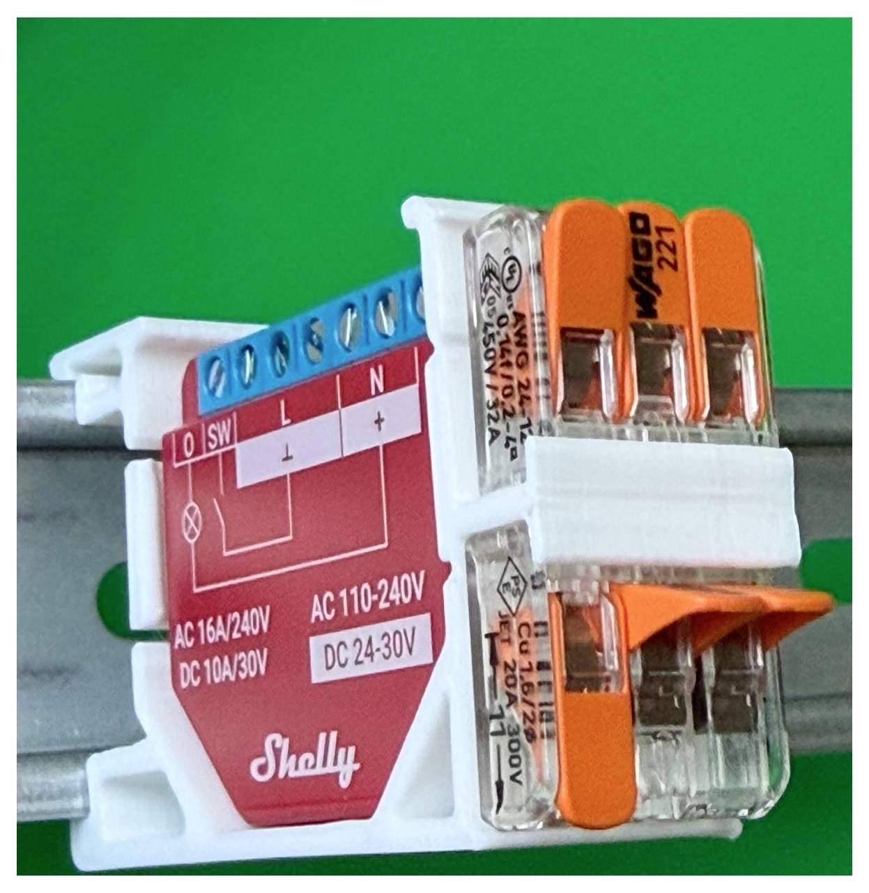 Nahaufnahme eines Shelly-Stromschaltmoduls mit blauen Schraubklemmen und orangefarbenen Steckverbindern, die auf einer Metallschiene montiert sind.