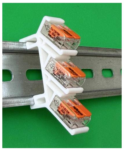 Drei elektrische Drahtsteckverbinder, die an eine Metallschiene vom Typ DIN-Schiene gegen einen grünen Hintergrund geclippt sind.