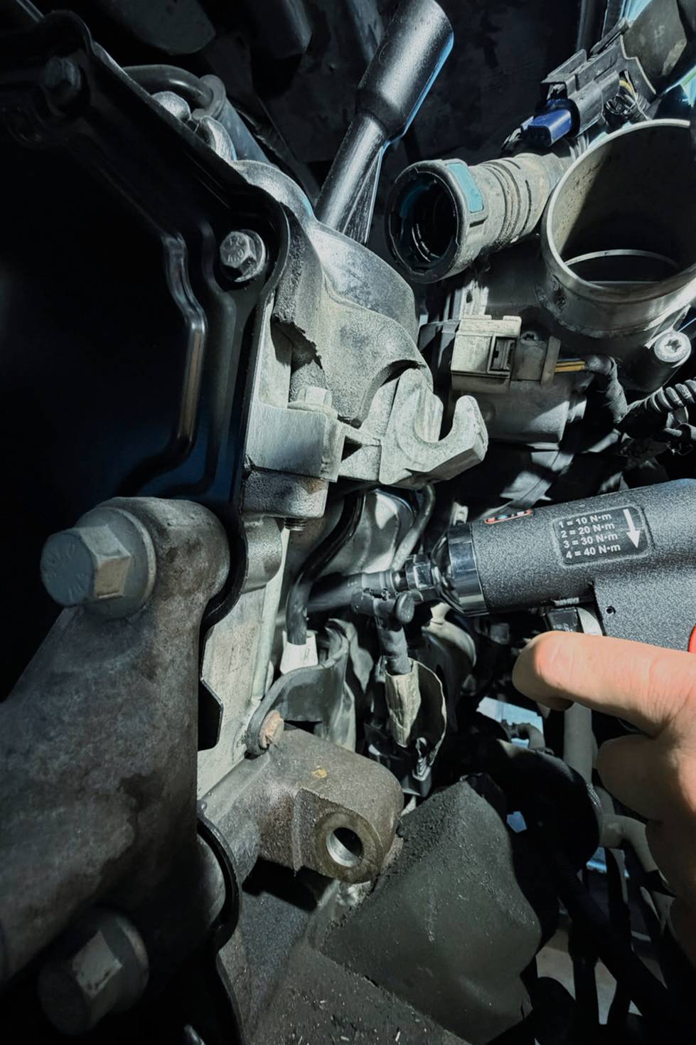 Nahaufnahme einer unter Reparatur befindlichen Motorkomponente, mit einer Hand, die auf ein kleines zylindrisches Teil in der überfüllten mechanischen Baugruppe zeigt.