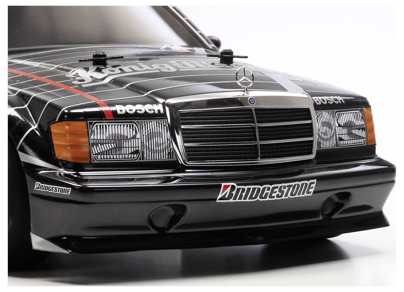 Vorderansicht eines schwarzen Mercedes-Benz Rennwagens mit Sponsorenlogos, einschließlich Bosch und Bridgestone, auf weißem Studiohintergrund.