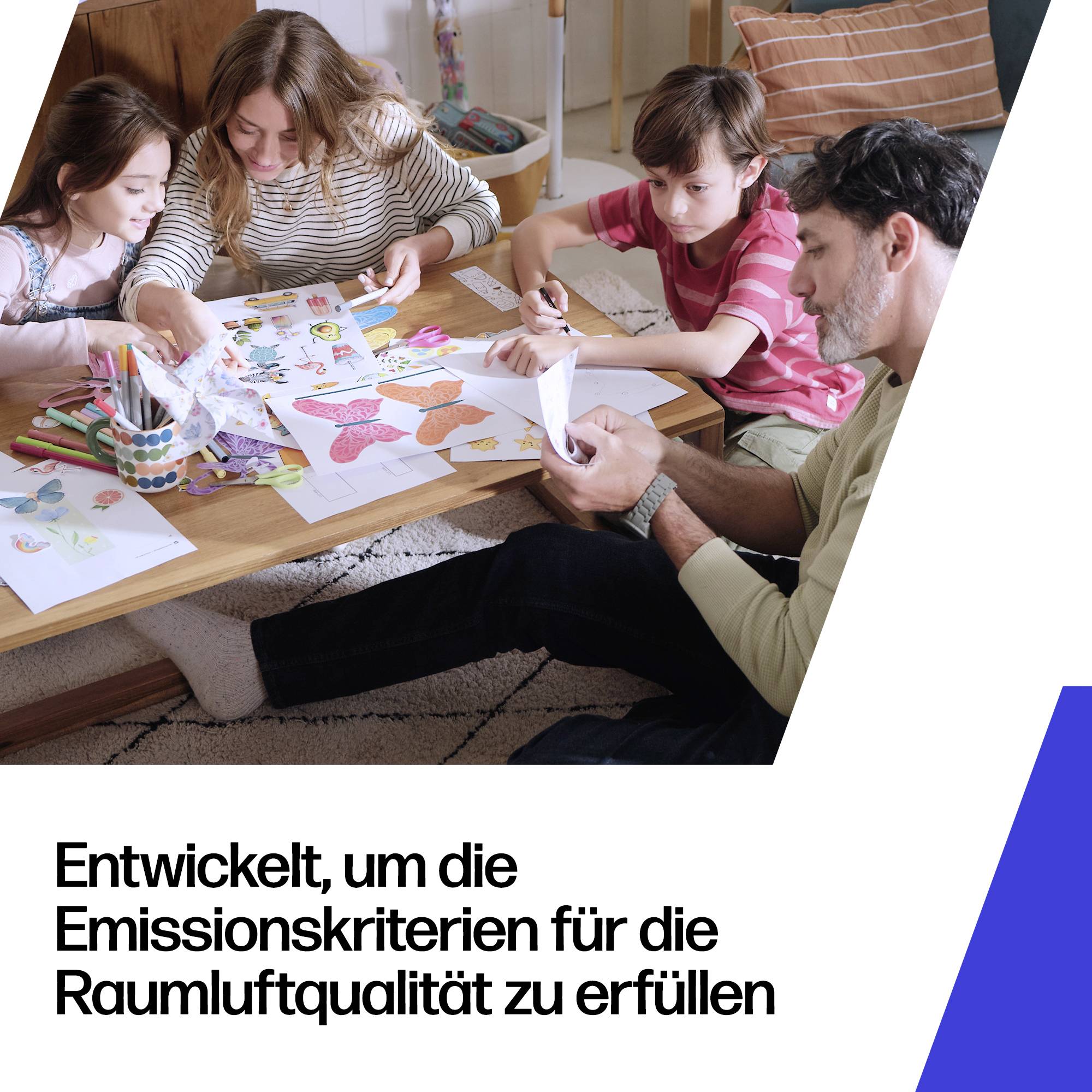 Familie an einem Tisch schneidet und bemalt Papier für ein kindgerechtes Bastelprojekt; Text lautet „Entwickelt, um die Emissionskriterien für die Raumluftqualität zu erfüllen“