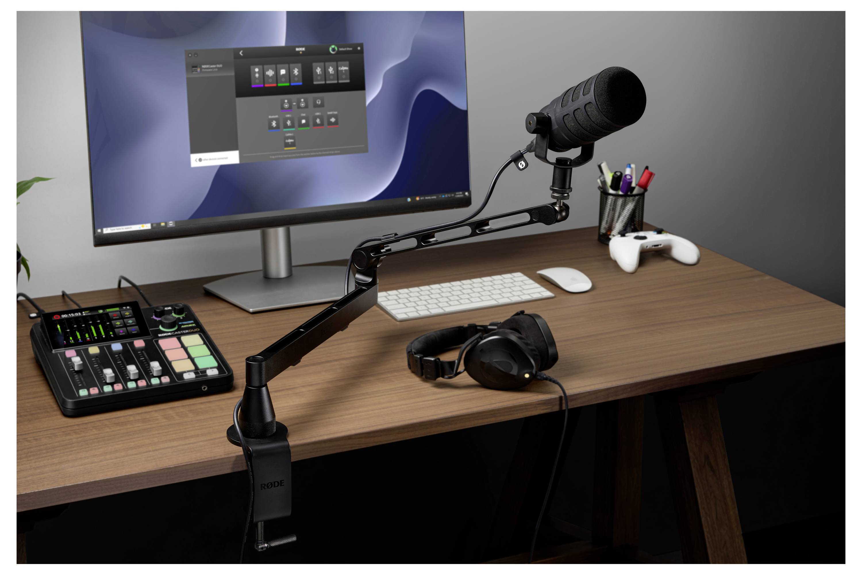 Desktop-Streaming-Setup mit Monitor, an einem Ausleger montiertem Mikrofon, Audio-Mixer, Tastatur, Maus, Kopfhörer und Gamecontroller auf einem Holzschreibtisch.