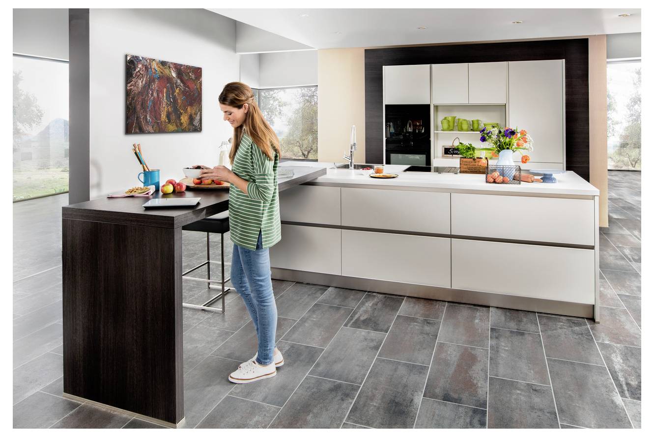 Frau bereitet Speisen auf einer Kücheninsel in einer modernen offenen Küche vor, mit Geräten, Obst und hellem zeitgenössischem Interieur.