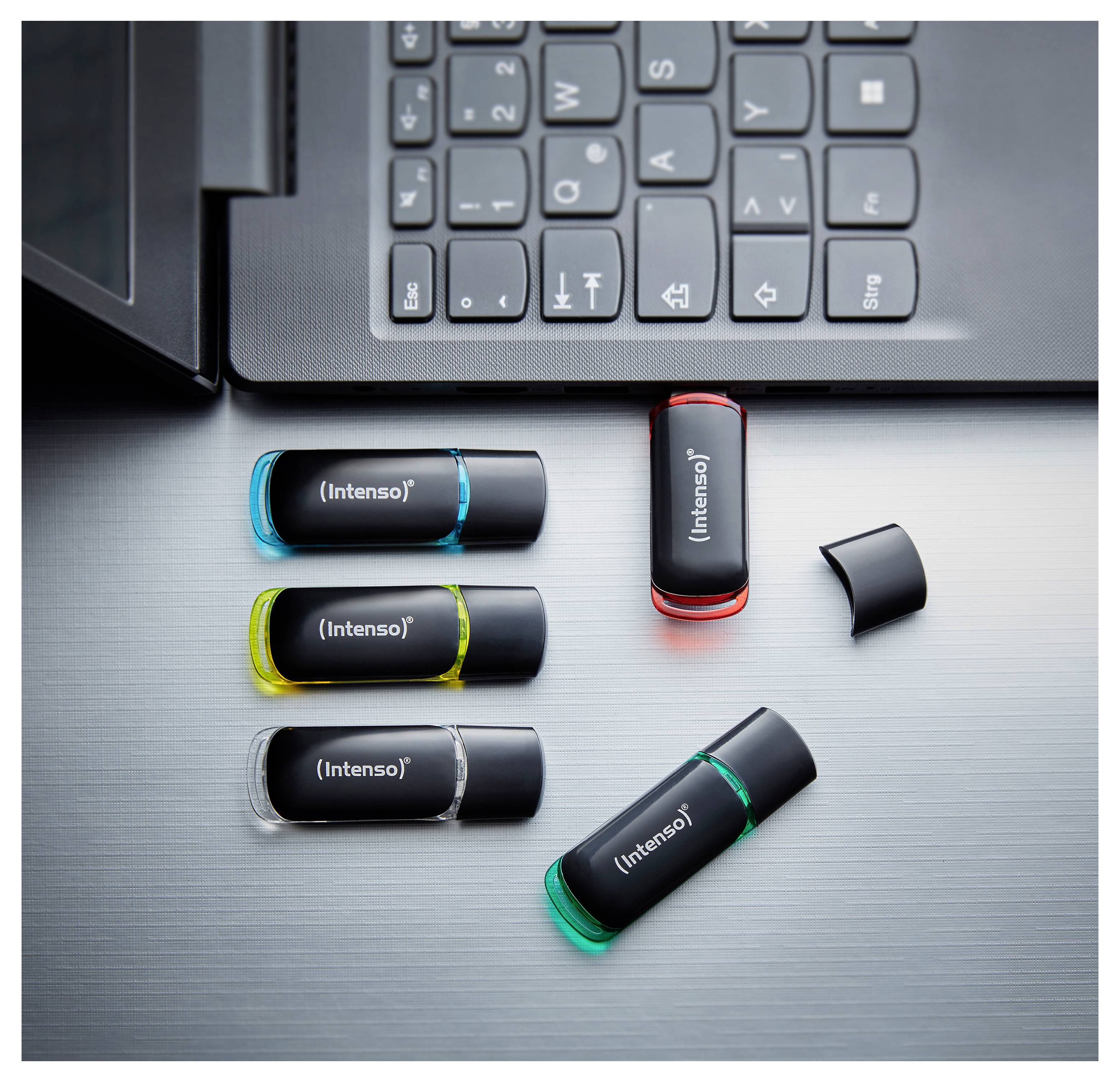 Mehrere Intenso USB-Speichersticks in verschiedenen Farben sind unterhalb einer Laptop-Tastatur angeordnet und deuten auf tragbare Datenspeicherung hin.