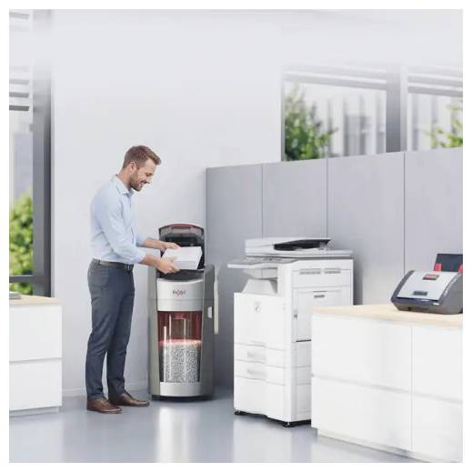Ein Mann in einem Büro füllt einen Reißwolf neben Druckern und einem Empfangstresen in einem modernen Arbeitsbereich mit Papier nach.