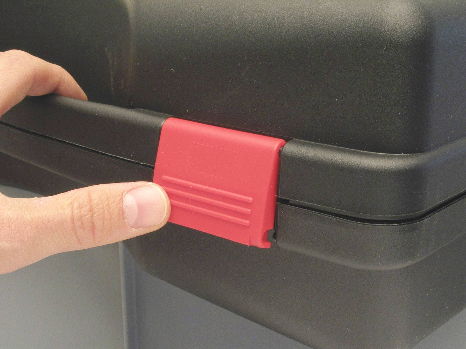 Eine Hand drückt einen roten Verschluss an einem schwarzen Koffer.