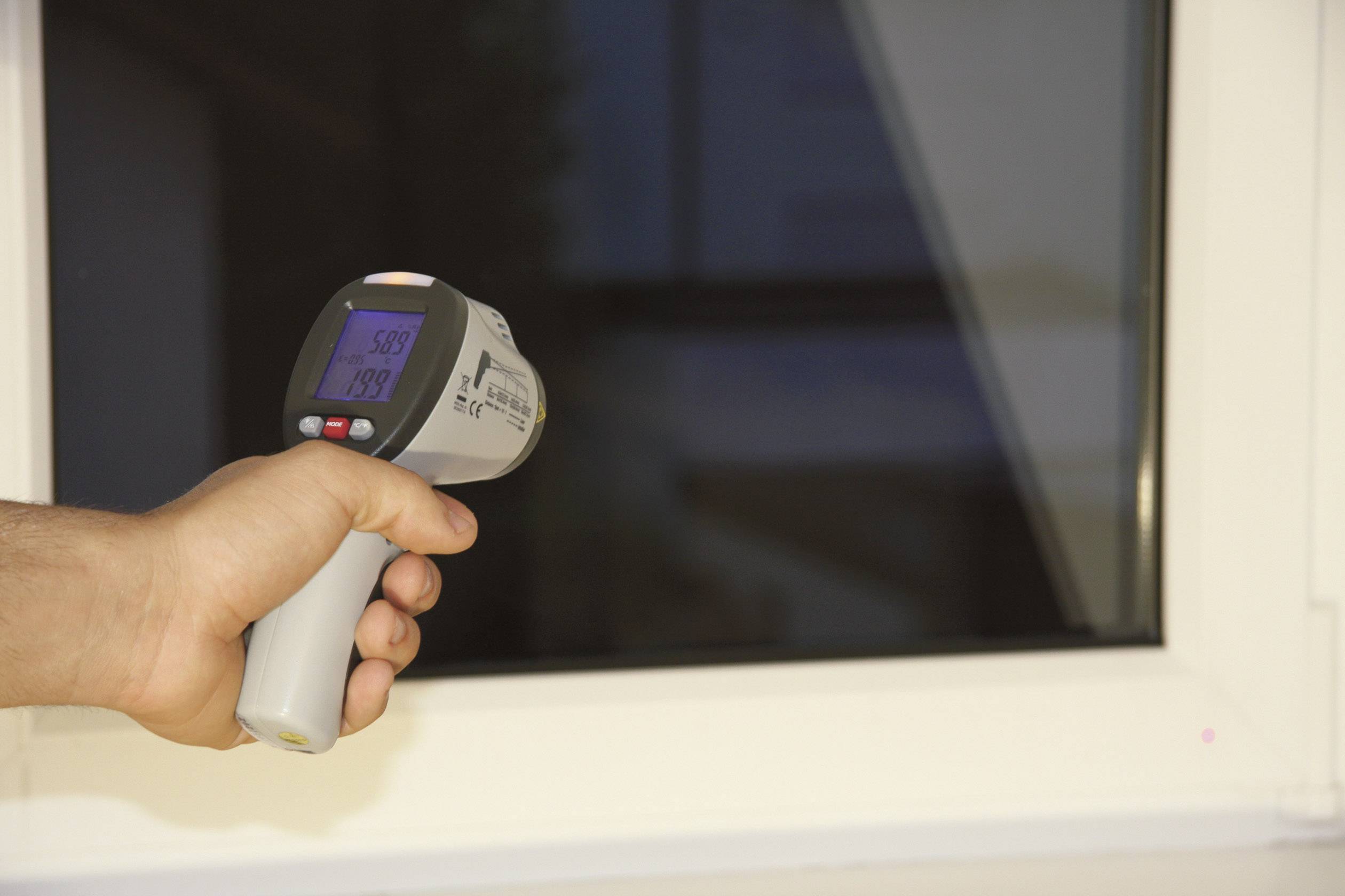 Eine Hand hält ein Infrarot-Thermometer vor ein Fenster, der Bildschirm zeigt 26,9 Grad an.