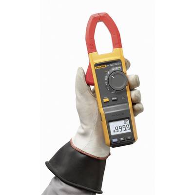 Eine Hand hält einen gelben digitalen Stromzangen-Multimeter mit rotem Greifer. Display zeigt "899,9", Schutzkleidung getragen.