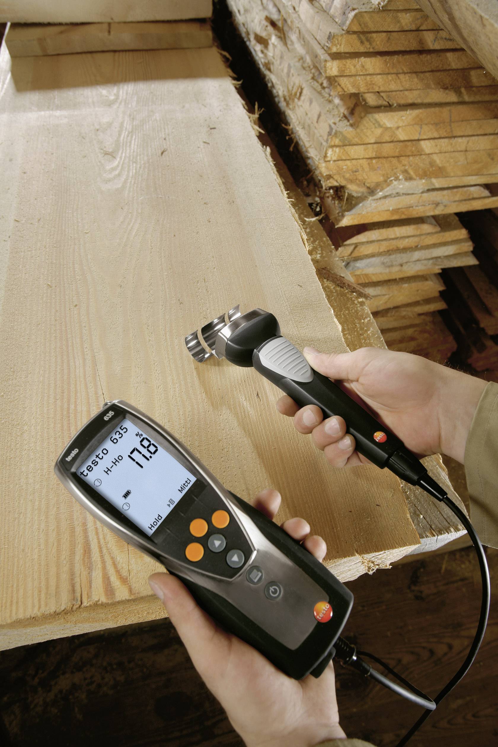 Eine Person misst den Feuchtigkeitsgehalt von Holz mit einem digitalen Messgerät auf einem Stapel Holzbretter.