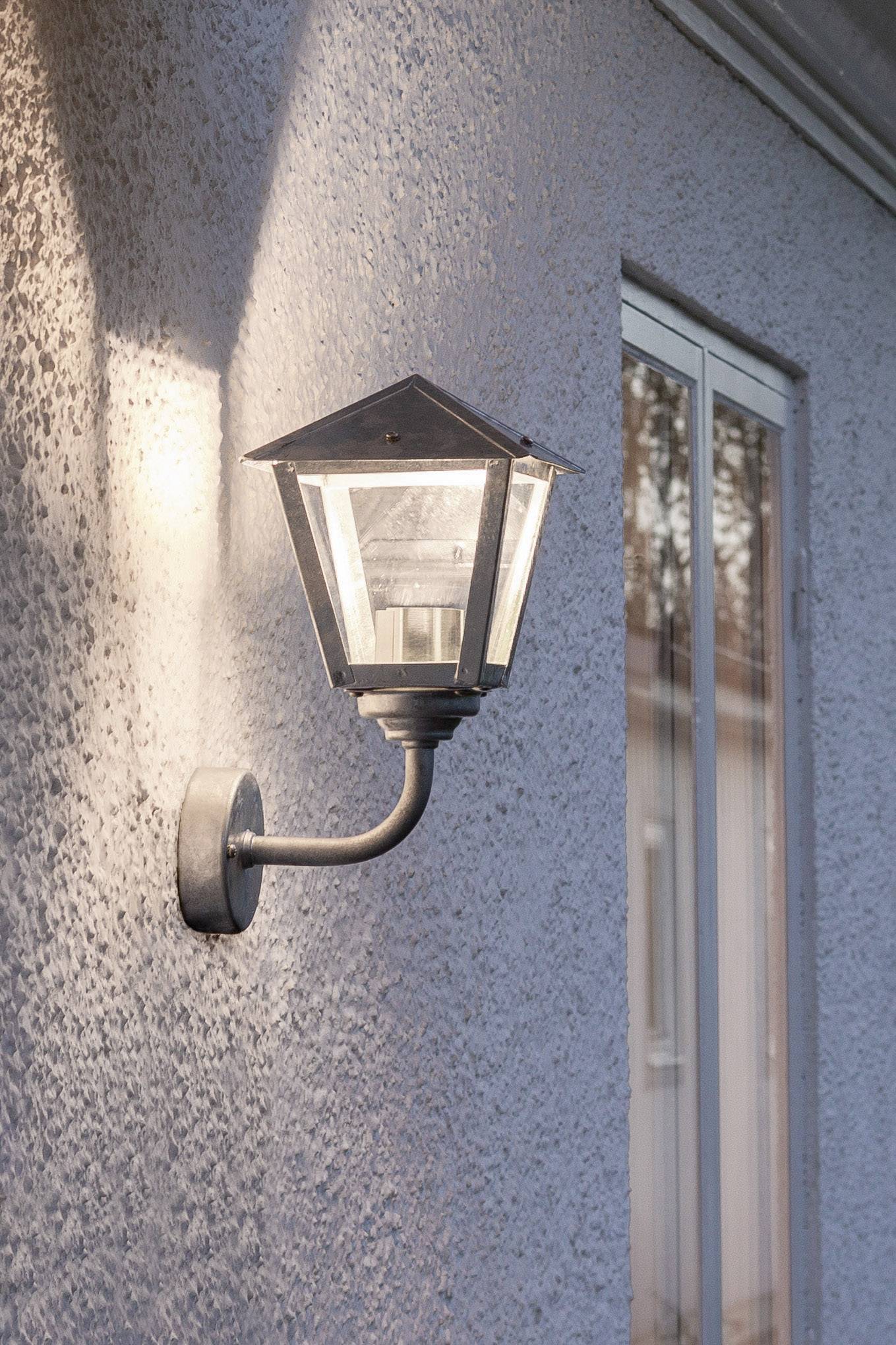 Außenlampe an einer weißen Wand, beleuchtet, neben einem Fenster.