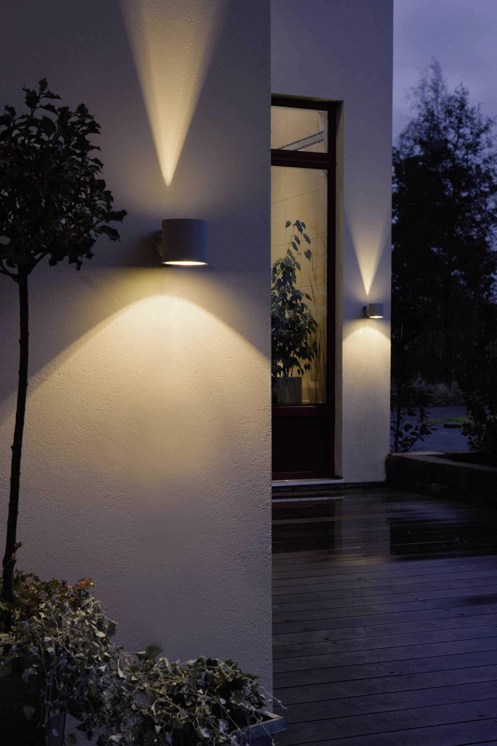 Moderne Außenbeleuchtung an einem Gebäude bei Dämmerung, Akzentlichter erhellen die Wand und schaffen eine einladende Atmosphäre auf der Terrasse.