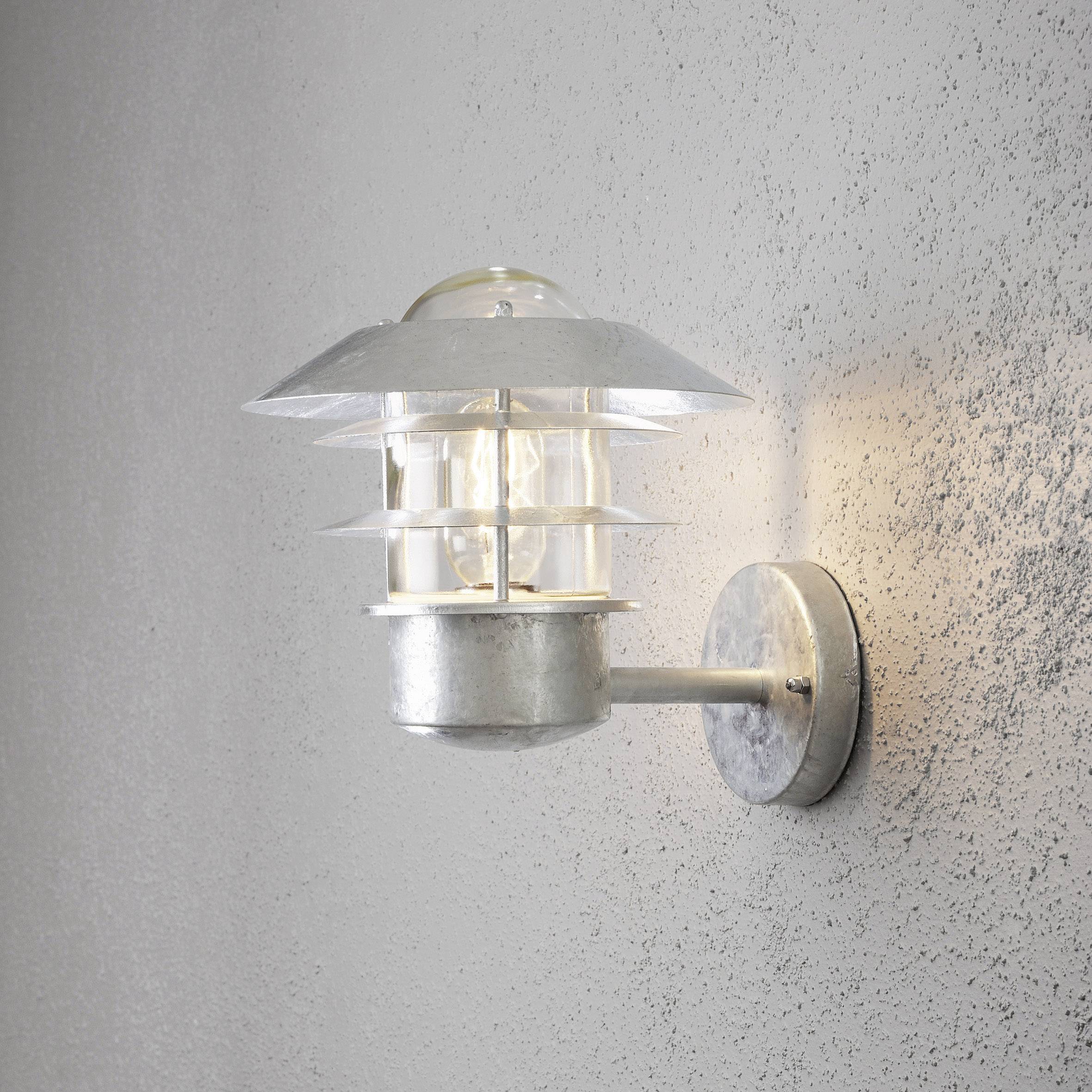 Außenwandlampe mit modernem, industriellem Design, montiert auf grauer Betonwand, strahlt warmes Licht aus.