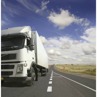 Lkw auf einer Landstraße, fährt bei blauem Himmel mit wenigen Wolken. Die Landschaft ist flach und leicht bewachsen.