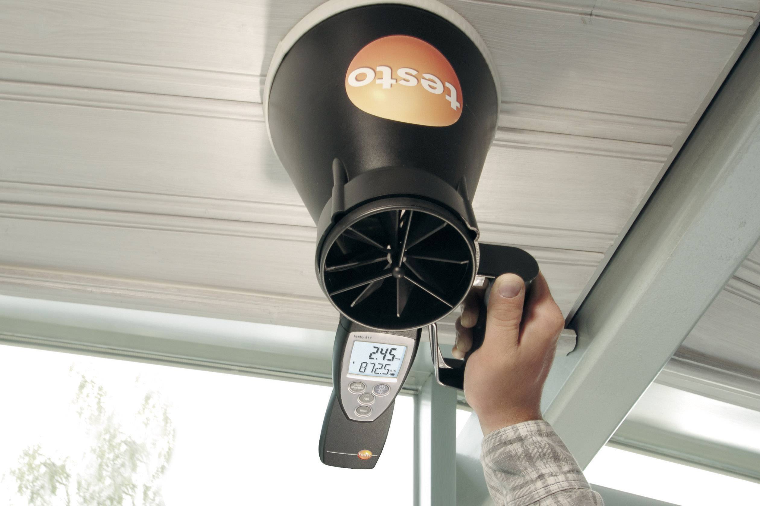 Eine Person hält ein Messgerät von Testo an einem Lüftungsauslass. Das Display zeigt 24,5 °C und 81,2 % Luftfeuchtigkeit.