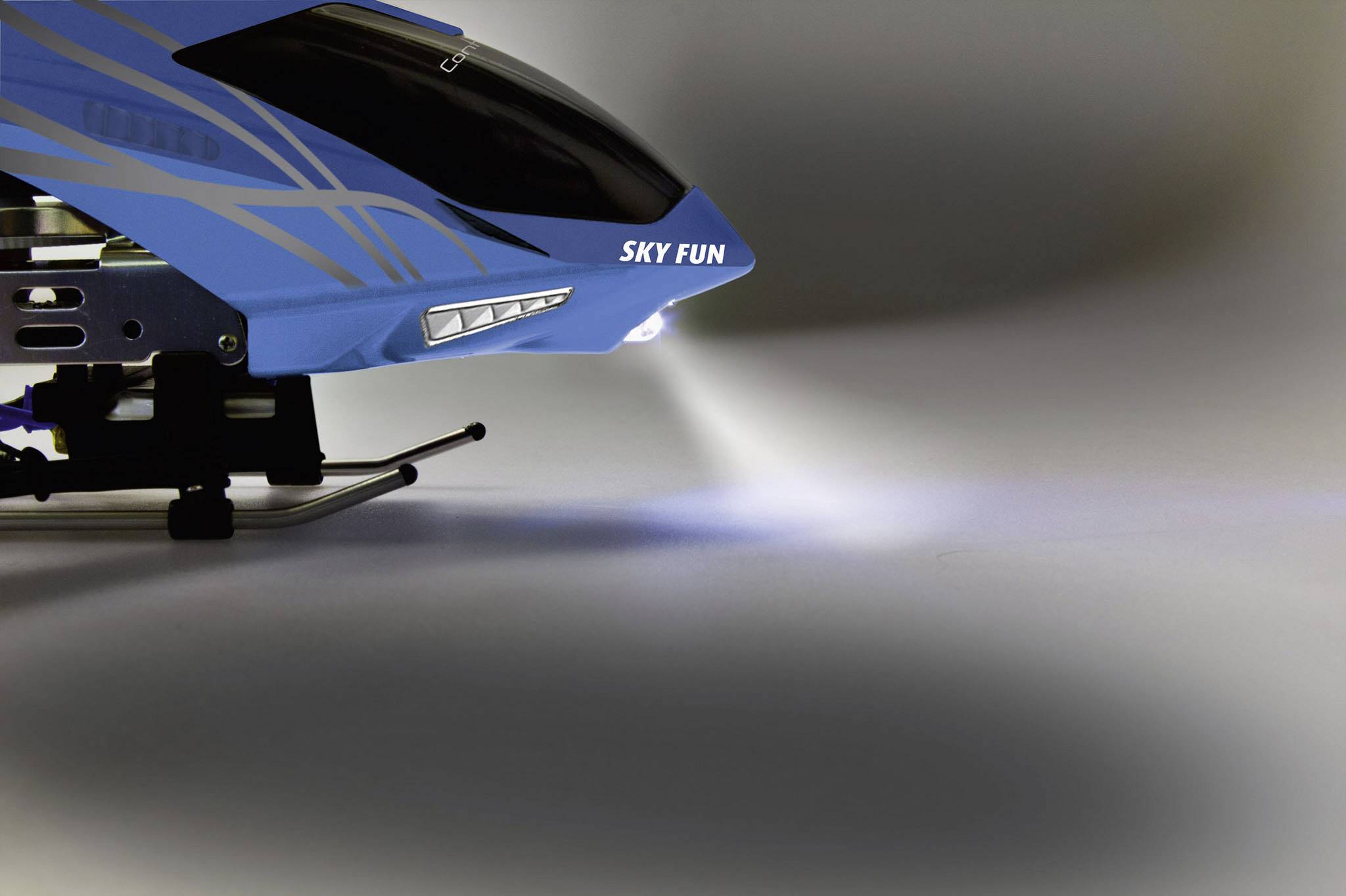 Ein blaues Modellflugzeug mit der Aufschrift 'SKY FUN' auf der Seite, beleuchtet den Boden mit einem weißen Lichtstrahl.