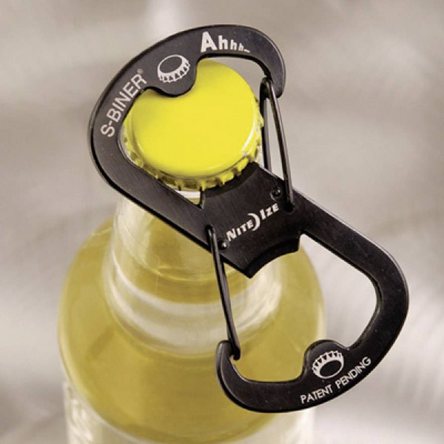 Ein Karabinerhaken mit integriertem Flaschenöffner, der eine Bierflasche öffnet. Aufschrift: 'S-BINER' und 'Ahhh'.