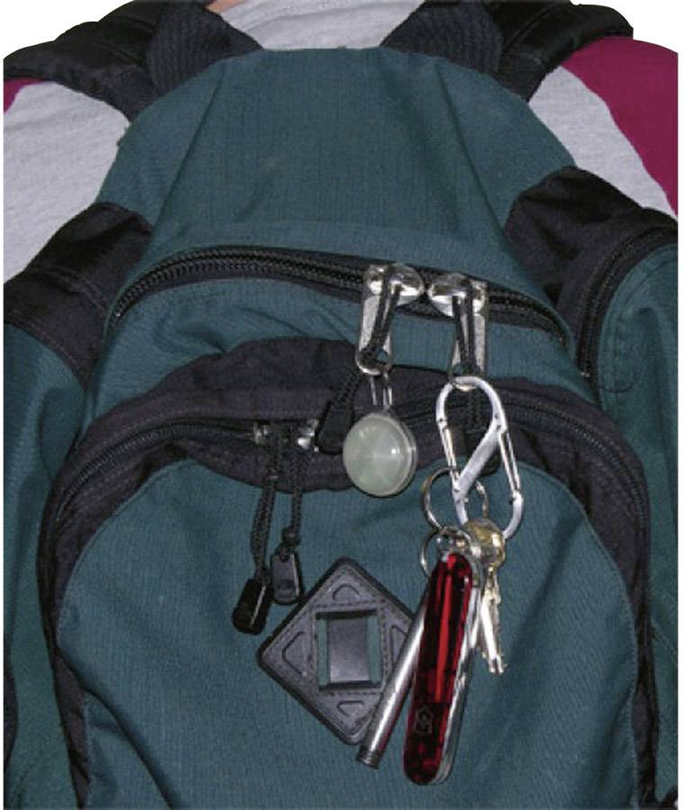Ein grüner Rucksack mit mehreren Reißverschlüssen und angebrachten Schlüsseln sowie einem Taschenmesser am oberen Reißverschluss.