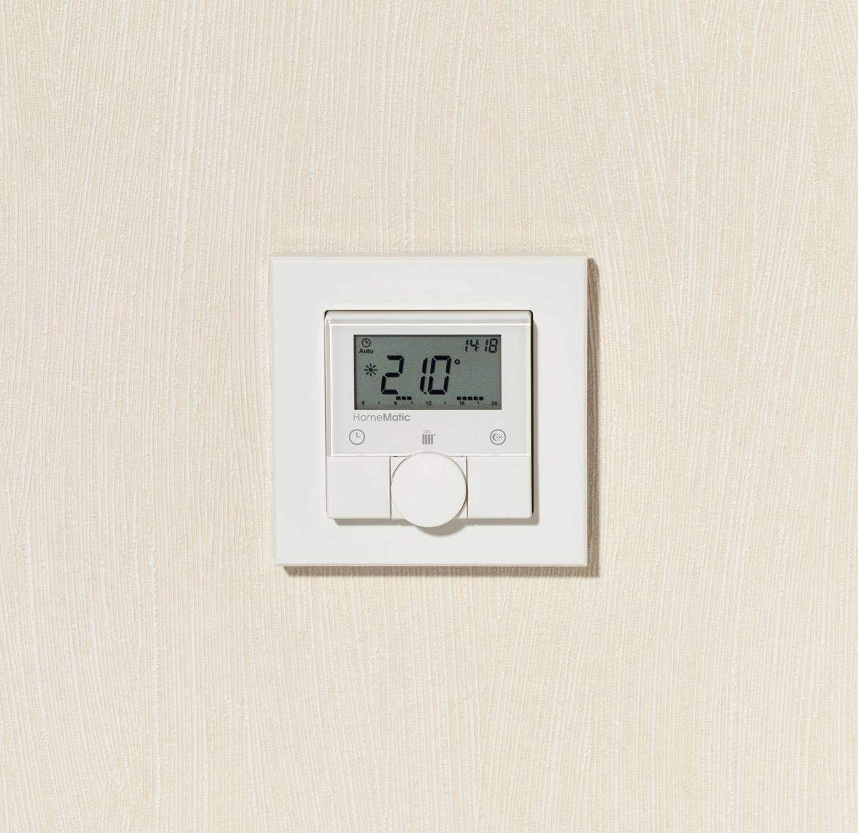 Ein moderner Thermostat an einer beigen Wand zeigt eine Temperatur von 21,0 Grad Celsius und die Uhrzeit 14:18 an.