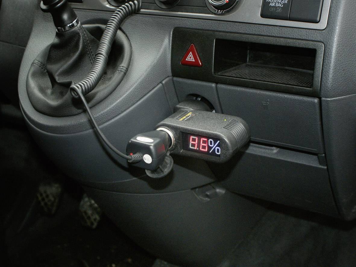 Ein Autoinnenraum zeigt einen Spannungsmesser in der Zigarettenanzünderbuchse, der '9,6%' anzeigt, nahe dem Schalthebel.
