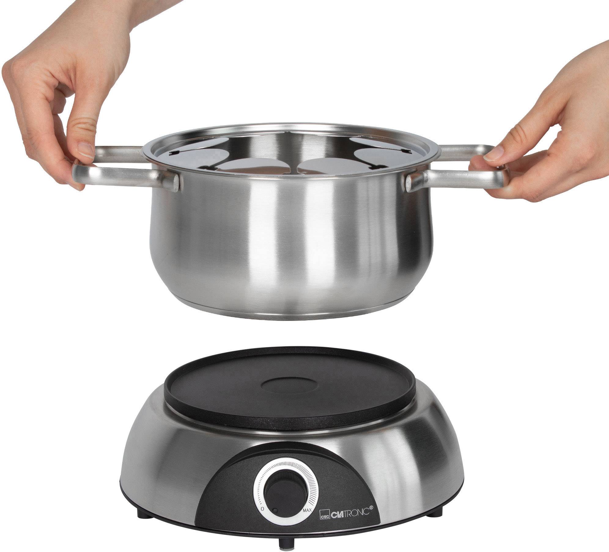 Eine Person hält einen silbernen Kochtopf über einer schwarzen elektrischen Herdplatte. Der Herd hat einen Drehknopf.