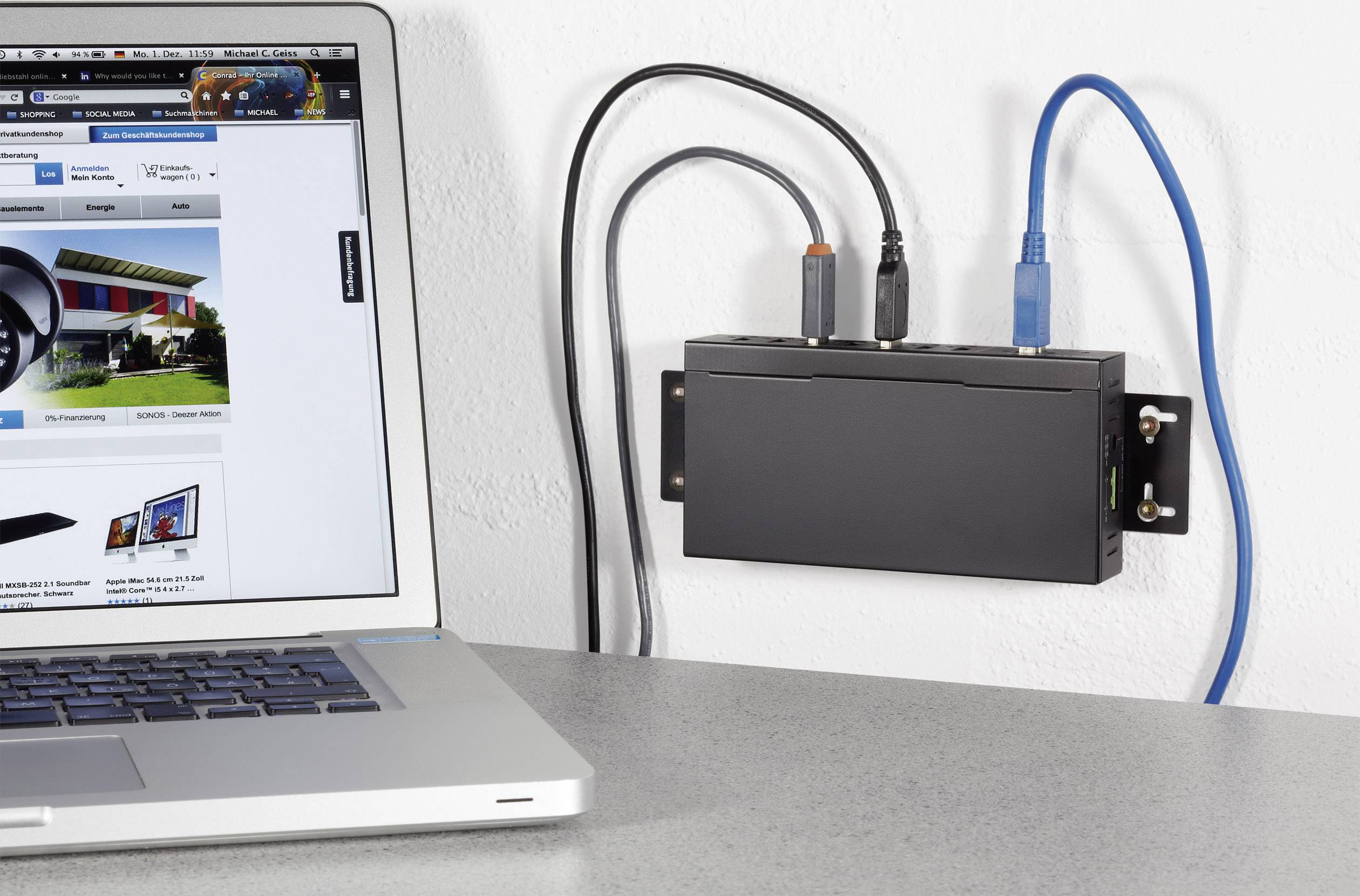 Ein Laptop zeigt eine Webseite mit einem Haus. Daneben an der Wand ist ein schwarzes Gerät mit mehreren Kabeln angeschlossen.