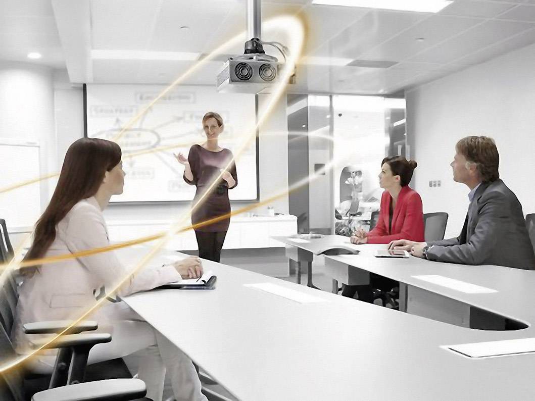 Eine Frau präsentiert an einem Beamer vor drei sitzenden Personen in einem modernen Konferenzraum. Rundum symbolisiert ein Lichtband Konnektivität.