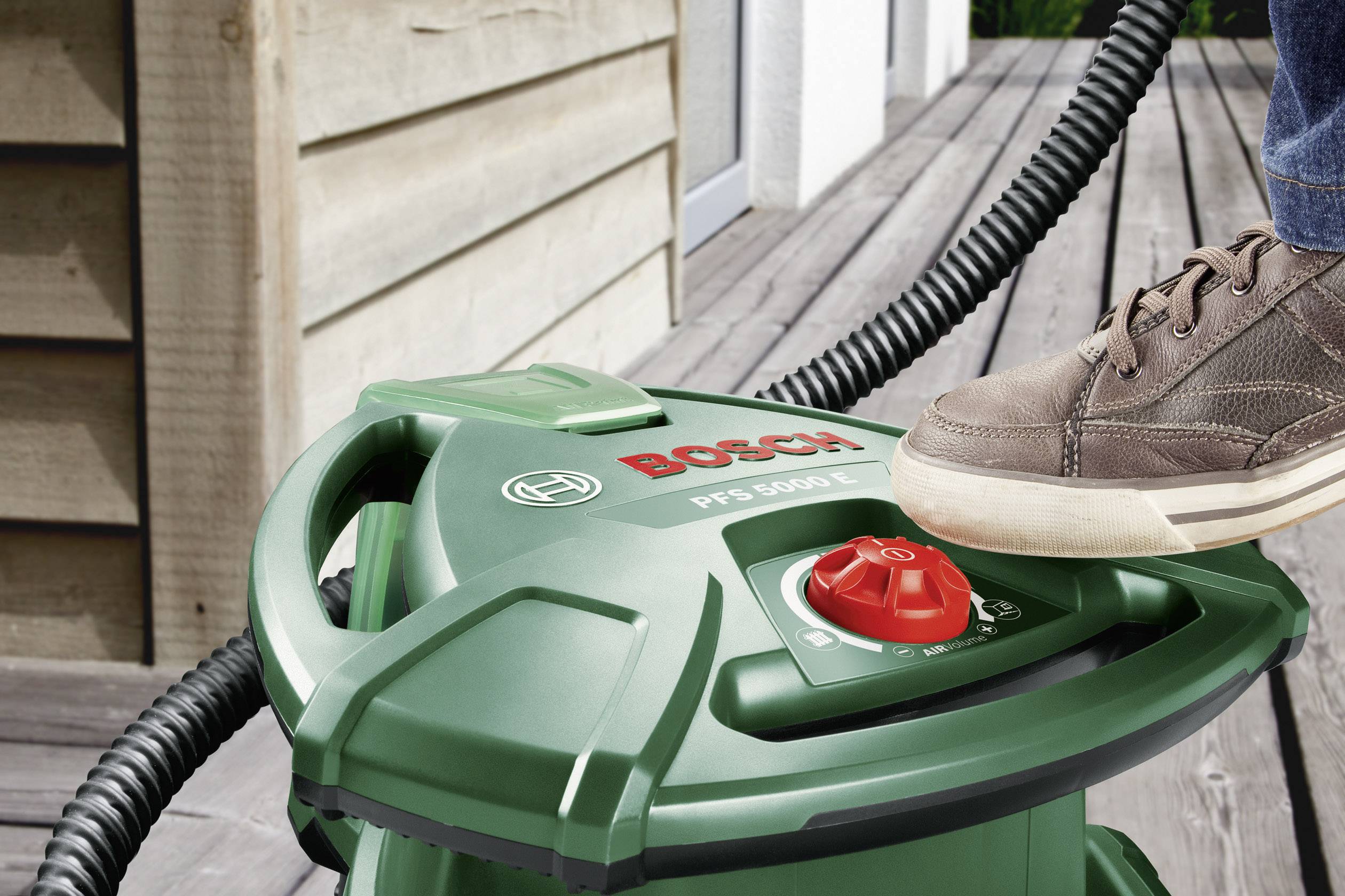Eine Person betätigt mit dem Fuß das Bosch PFS 5000 E Farbsprühsystem auf einer Terrasse.