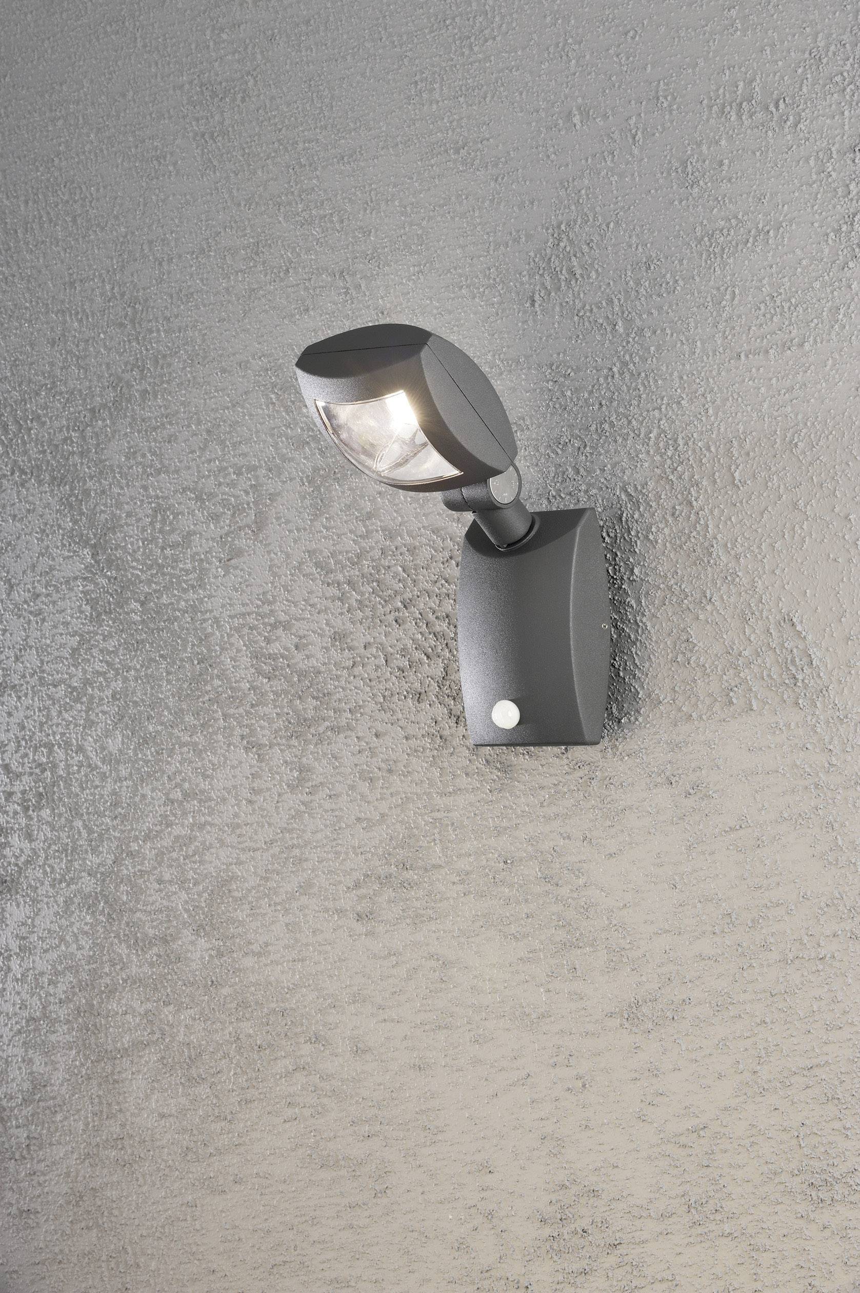 Wandleuchte mit modernem Design und verstellbarem Spot, montiert auf einer strukturierten grauen Wand, leuchtet nach unten.