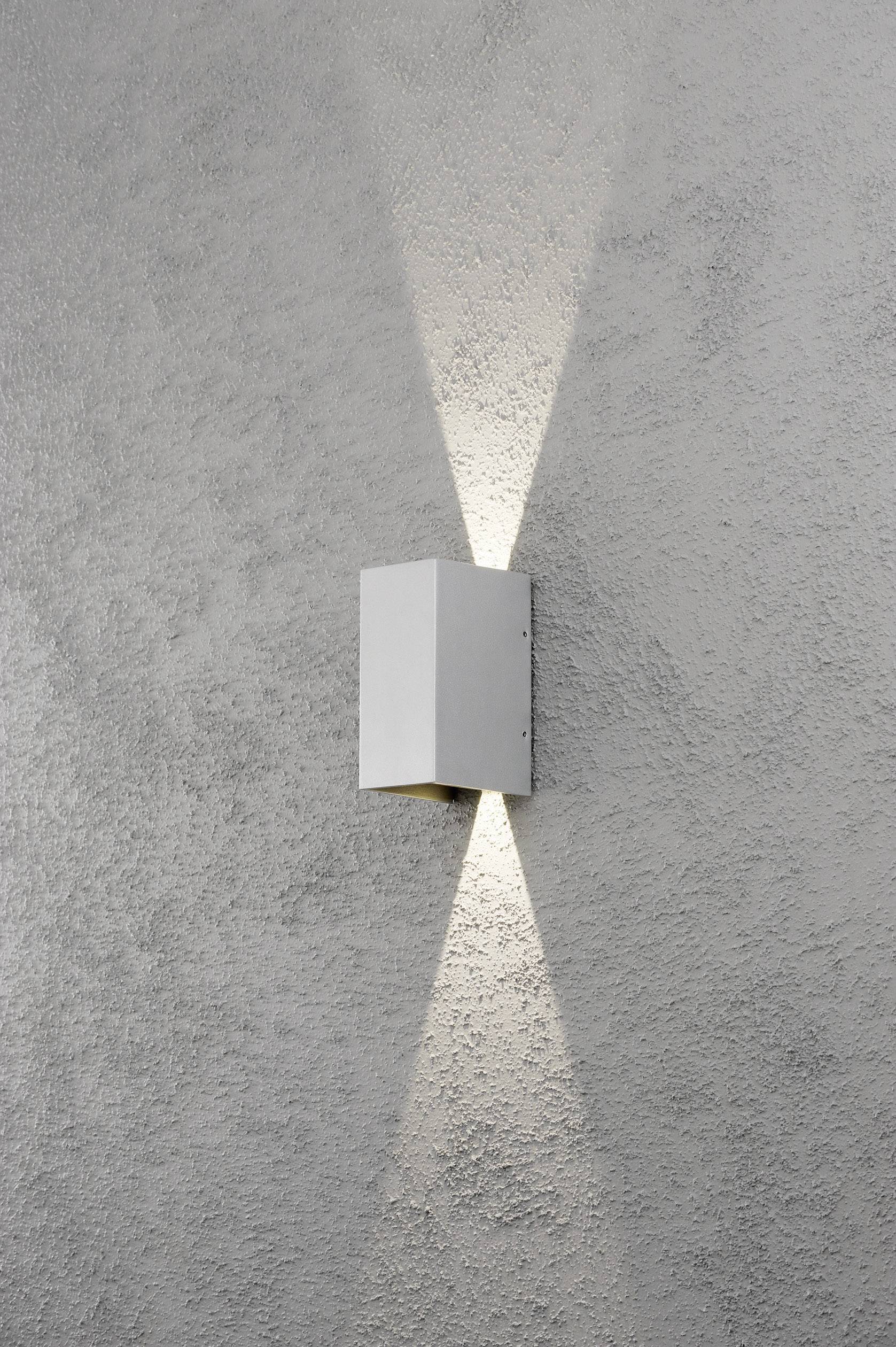 Eine moderne, weiße Wandleuchte an einer grauen Wand. Die Lampe strahlt Licht sowohl nach oben als auch nach unten aus, erzeugt konzentrische Lichtkegel.