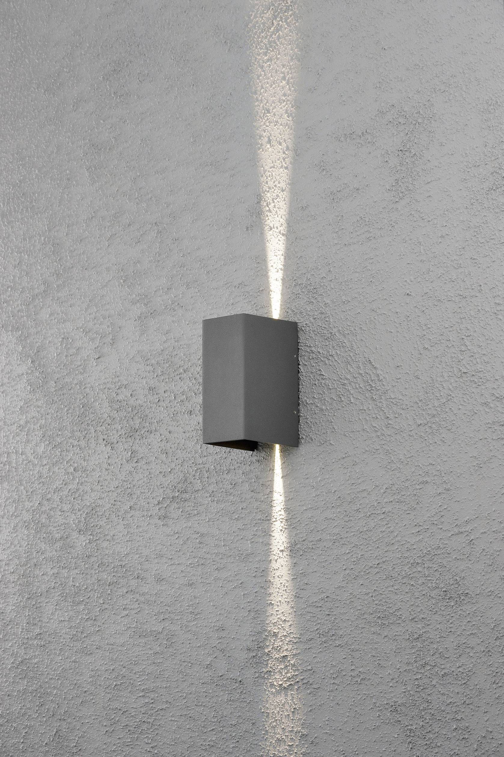 Graue Außenwandlampe strahlt Licht nach oben und unten auf eine strukturierte, graue Wand und erzeugt ein symmetrisches, vertikales Muster.