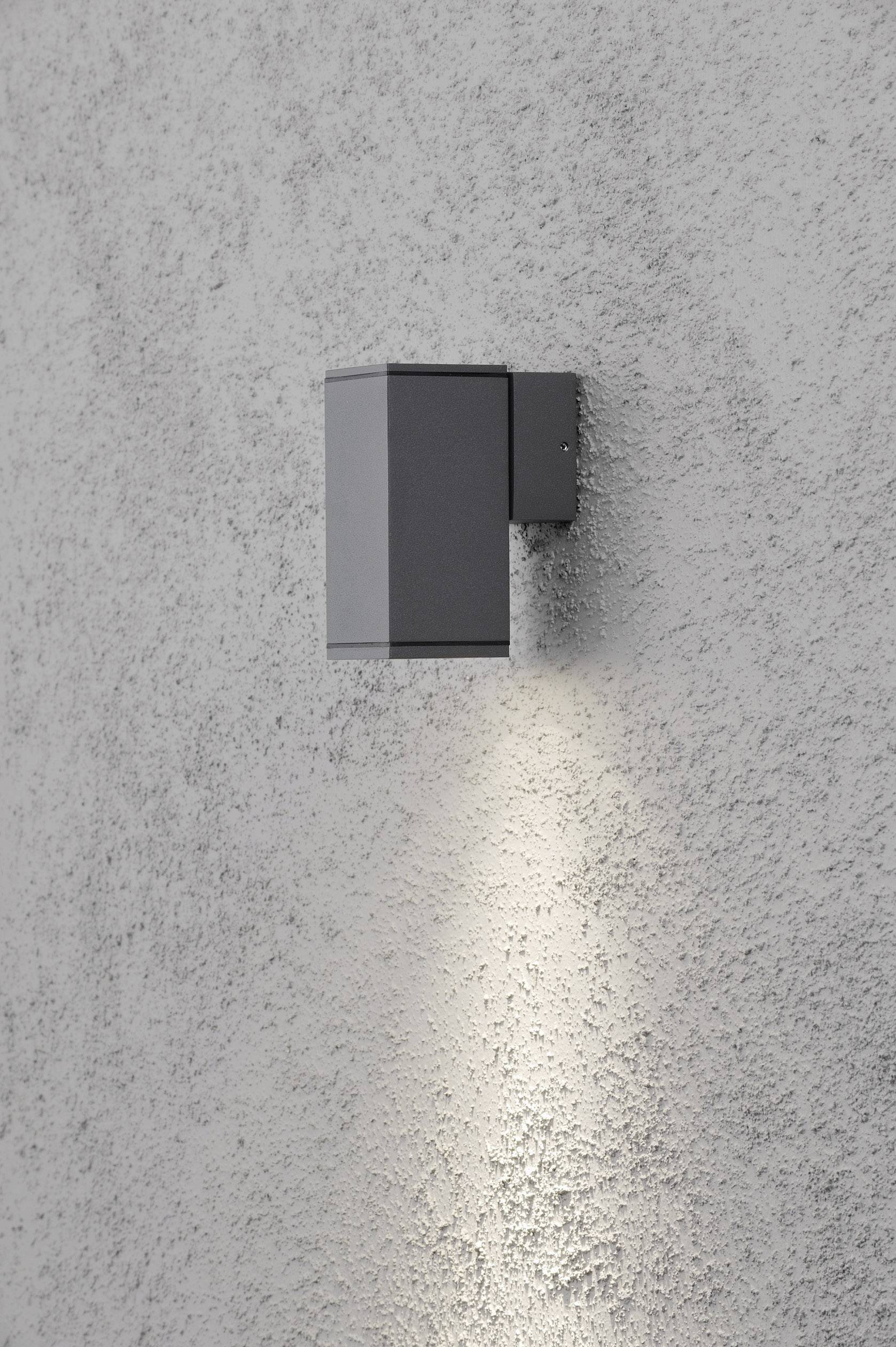 Außenleuchte an grauer Wand, leuchtet nach unten und erzeugt einen schmalen Lichtkegel. Modernes, minimalistisches Design.