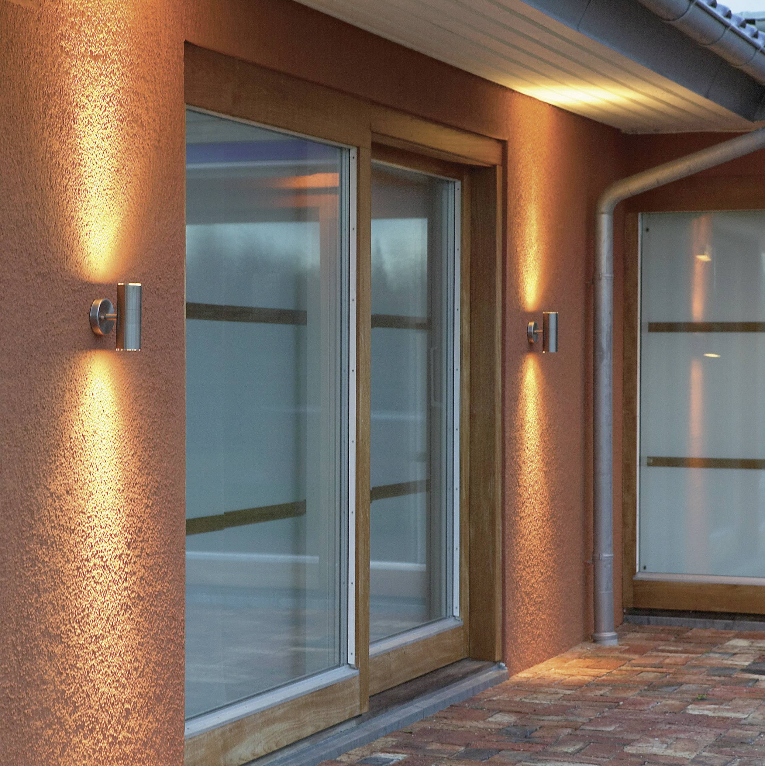 Beleuchteter Terrassenbereich mit Glastüren, modernen Wandlampen und gemauertem Bodenbelag, der abends ein warmes Ambiente schafft.
