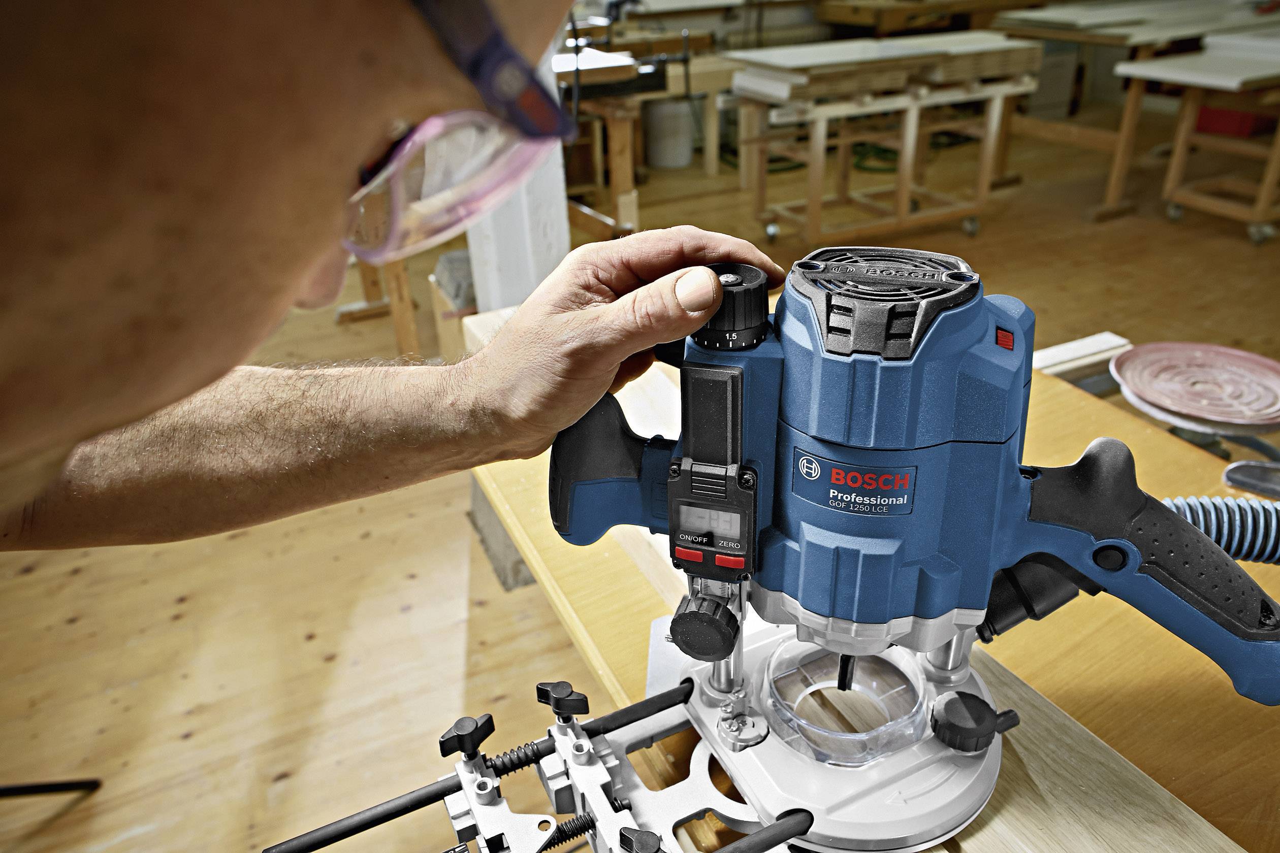 Eine Person verwendet eine blaue Bosch-Oberfräse, um präzise Holzarbeiten in einer Werkstatt durchzuführen.