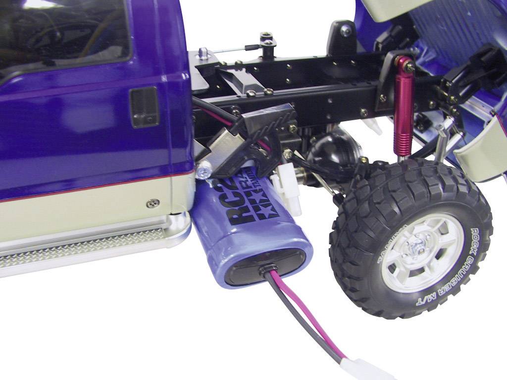 Ein ferngesteuertes Modellauto mit sichtbarem Fahrwerk und Akku. Der Akku ist angeschlossen und das Auto hat große, profilierte Reifen.