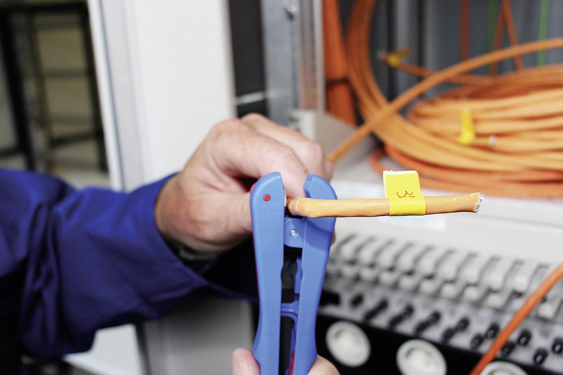 Eine Person verwendet ein Werkzeug, um ein orangenes Kabel in einem Netzwerkverteiler zu bearbeiten. Kabel sind ordentlich aufgerollt.