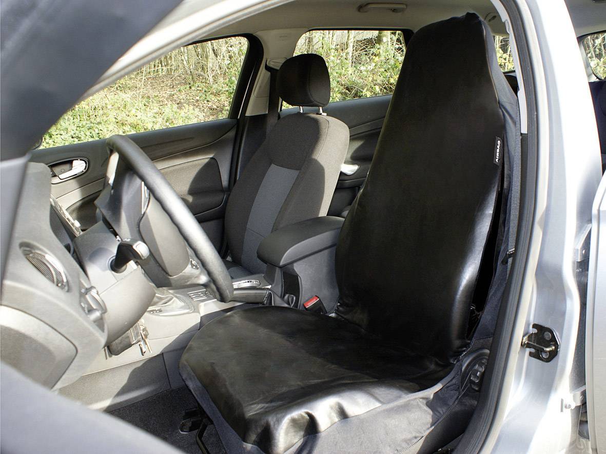 Auto-Innenraum mit einem schwarzen Schonbezug auf dem Fahrersitz. Der Beifahrersitz ist nicht bedeckt. Umgebung bewaldet.