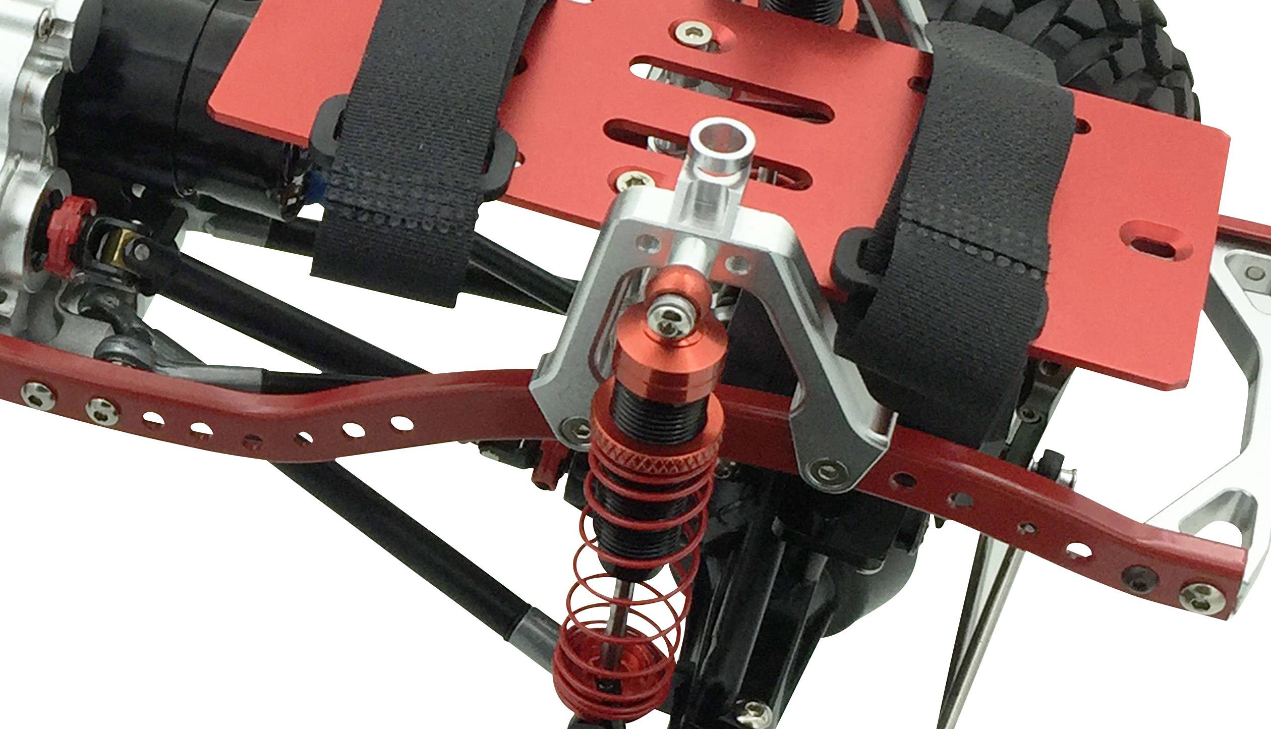 Nahaufnahme eines ferngesteuerten Fahrzeugchassis mit roten Stoßdämpfern und Halterungen. Sichtbar sind Metall- und Kunststoffkomponenten.