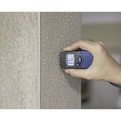 Eine Hand hält ein elektrisches Feuchtigkeitsmessgerät an einer Betonwand. Das Display zeigt den Feuchtigkeitsgehalt der Wand.