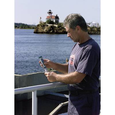Ein Mann steht auf einem Boot und betrachtet ein Objekt in seinen Händen. Im Hintergrund ist ein Leuchtturm auf einer kleinen Insel sichtbar.