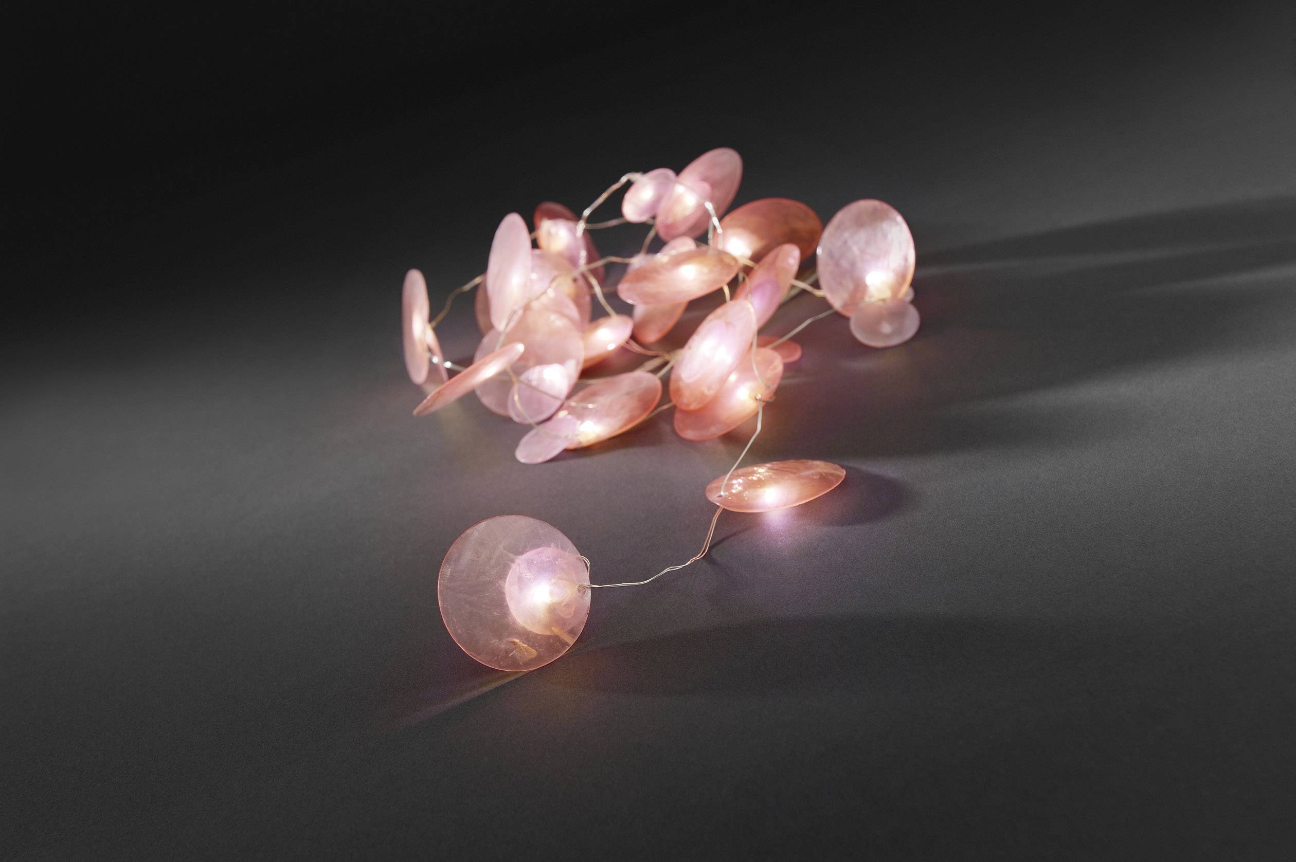 Lichterkette mit rosa Scheiben liegt in kreativem Muster auf grauem Hintergrund, leuchtet sanft.