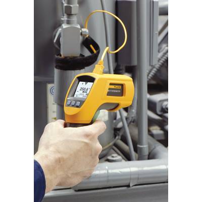 Eine Hand hält ein Infrarot-Thermometer, das eine Temperatur von 25,6 Grad Celsius misst, vor einer industriellen Maschine.