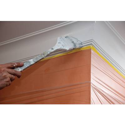 Ein Pinsel trägt weiße Farbe auf die oberste Kante einer orange gestrichenen Wand auf. Eine gelbe Linie dient als Markierung.
