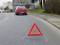 Rotes Auto und Warndreieck auf einer Straße, das auf eine mögliche Panne oder Gefahr hinweist.